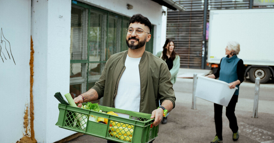 Ein junger Herr trägt eine grüne Kiste mit Obst und Gemüse 